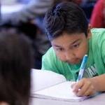 An elementary student writes in a notebook in a classroom